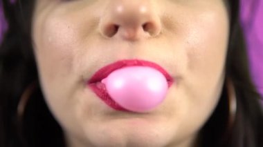 Mor arka planı çiğneyen büyük pembe sakız üfleyen kız.