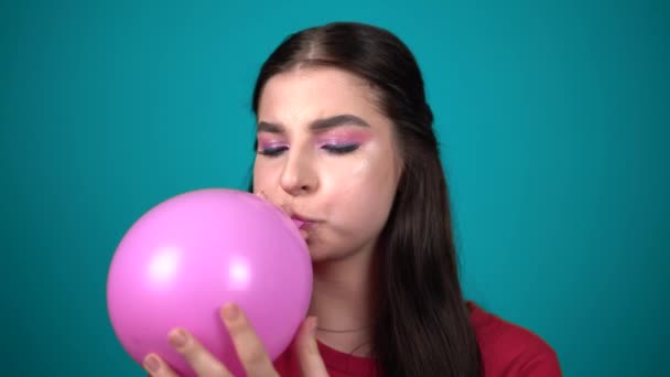 Genç bir kadın mavi arka planda izole edilmiş bir balonu şişiriyor. — Stok video