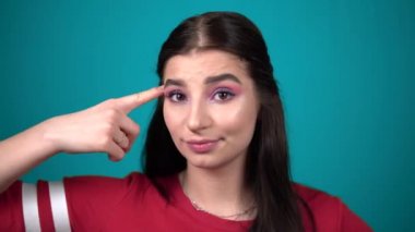 Genç bir kadın şakağına parmağını çeviriyor, kameraya bakıyor, duygusal bir portre.