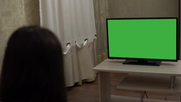 Женщина сидит на диване, смотрит телевизор Зеленый экран макет. Вечер дома — стоковое видео