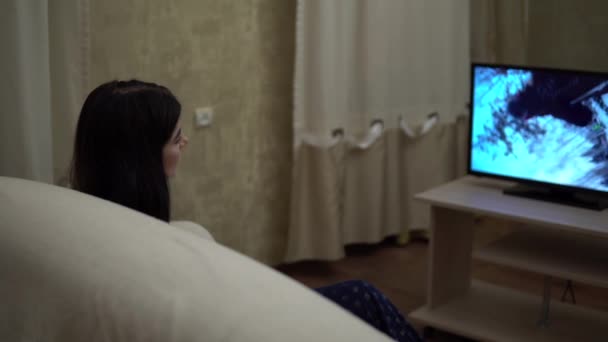 Жінка дивиться телевізор на дивані в затишній вітальні, що розслабляється вдома на карантині — стокове відео