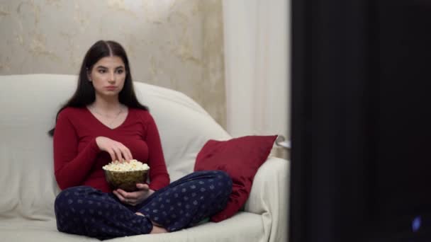 Γυναίκα χαλαρώνοντας στον καναπέ βλέποντας τηλεόραση τρώει ταινίες ποπ κορν ζεστό σπίτι το βράδυ — Αρχείο Βίντεο