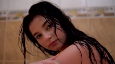 Banyodaki çıplak ve ıslak kız kameraya bakıyor. Rimel sürmüş, ıslak saçlar dramatik.