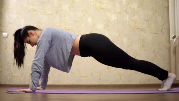 Спортивная женщина остается на доске на руках тренировки на дому на тряпке для практики йоги — стоковое видео