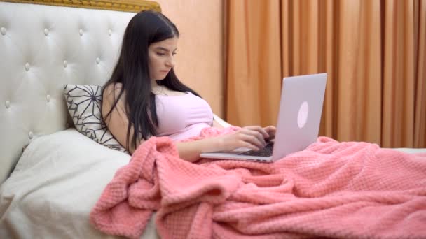Yatakta çalışan serbest çalışan bir kadın, rahat bir ev, dizüstü bilgisayar mesafesini kullanarak çalışıyor. — Stok video