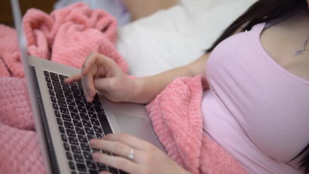 Женщина в постели печатает на клавиатуре, с помощью ноутбука, дистанционной работы или учебы — стоковое видео