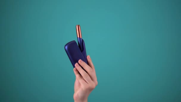 Mão segure e-cigarro no fundo azul, dispositivo de fumar, aquecimento da vara do tabaco — Vídeo de Stock