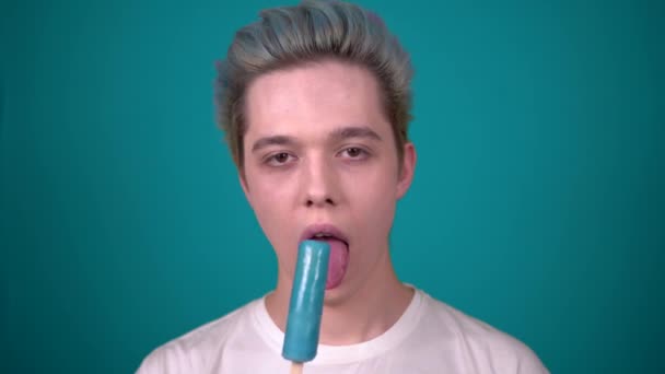 Joven hombre feliz comiendo helado disfrutando de dulces aislados sobre fondo azul — Vídeos de Stock