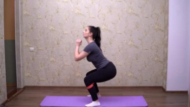 Çömelme hareketleri yapan bir kadın, evde kilo vermek için spor antrenmanı, spor lastiği.