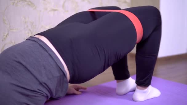 Женщина занимается фитнесом дома, худеет, спортивные упражнения с резиной — стоковое видео