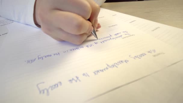Форма экзамена на столе в классе, студент сдает экзамены, рука с ручкой крупным планом — стоковое видео