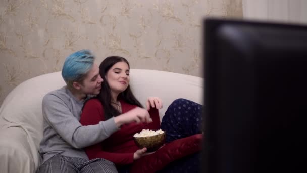 Alegre hombre y mujer viendo la televisión comiendo palomitas de maíz riendo juntos, acogedor hogar — Vídeo de stock