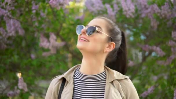 Jonge vrouw kijken naar camera, lila achtergrond, lente wandelen — Stockvideo