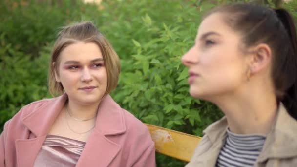 Женщины-друзья разговаривают в парке, сидят на скамейке, концепция дружбы — стоковое видео