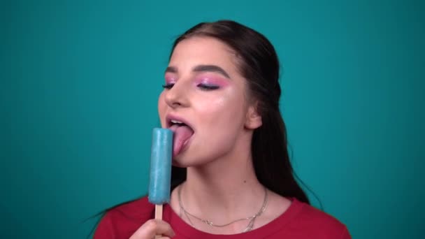 Mujer joven comiendo jugo helado disfrutando de dulces aislados sobre fondo azul — Vídeos de Stock