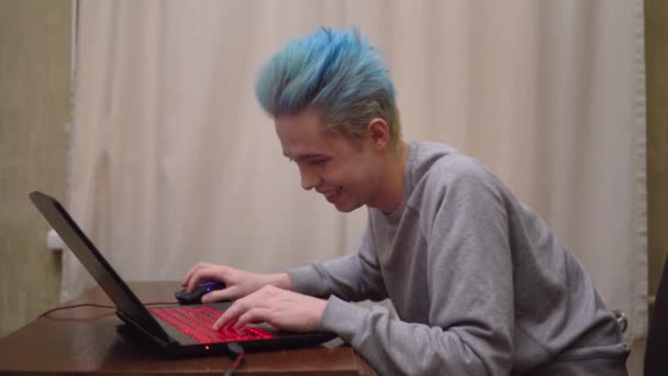Играет в компьютерную онлайн-игру, улыбается, выигрывает, сосредоточен на игре, синие волосы — стоковое видео