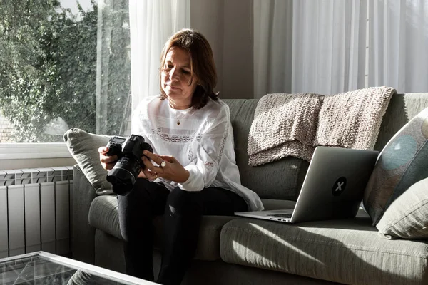 白いシャツを着たライトアイの茶色の髪の女性は 自宅のソファから快適にノートパソコンで作業しています 彼女は社会的孤立に準拠している ロイヤリティフリーのストック画像