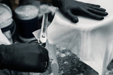 Atölyesinde beyaz gömlek şekillendiricisi ve siyah eldiven kullanarak sörf tahtası üretiyor. Tahtasını yapmak için beyaz köpük, fiberglas bez ve aletler kullanıyor..