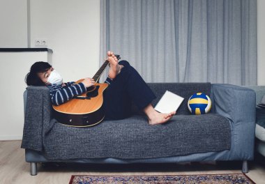 Ağız maskesi takan genç Asyalı çocuk evde sıkılıyor (konsept ev karantinası)