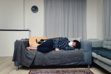 Evde karantina altında küçük bir Asyalı çocuk, ağız maskesi takıyor ve kanepede uyuyor (konsept ev karantinası)