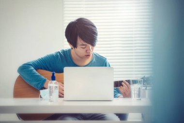 Corona virüsü salgını nedeniyle evde karantina altında gitar çalan yakışıklı Asyalı çocuk (konsept)