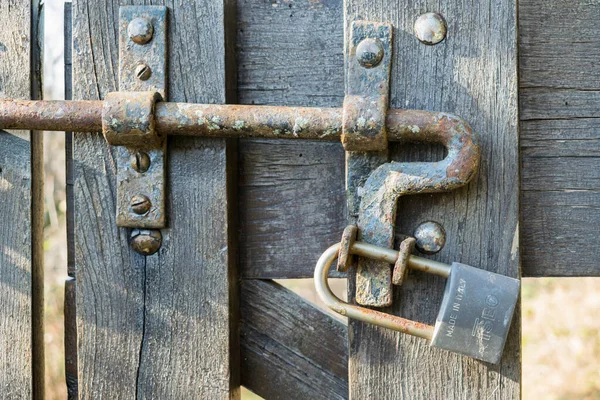 details of a closed wooden gate with old rusty padlock in a sunny day