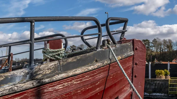The front end of a red ship. old red wooden ship. rope is tied to ship. blue sky with white clouds