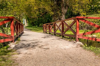 Küçük bir nehrin üzerindeki kırmızı köprü. Arka planda pembe bir rhododendron ve büyük yaşlı bir ağaç var..