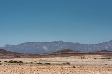 Brandberg dağı mavi gökyüzünün altında, kurak ve kumlu bir önplanı var. Namibya