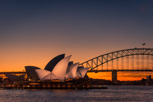 Sydney, New South Wales / Australia - May 17th 2016: Sydney Opera House lit up with light at night time with Harbour Bridge to the right and the last red and orange colours of sunset in the background
