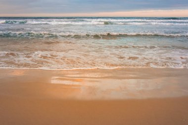 Plettenberg Körfezi sahilinde dingin dalgalar kopuyor ve günbatımı renklerini yansıtıyor. Bahçe Yolu, Batı Burnu, Güney Afrika