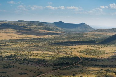Ufuktaki tepelere doğru uzanan uçsuz bucaksız kurak çalı düzlükleri vadi boyunca uzanan tek bir yol. Pilansberg Oyun Rezervi, Güney Afrika