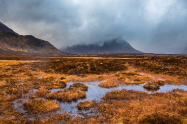 Buachaille Etive Mor, bulutlarla kaplıydı. Önünde bataklık suyu ve çimen vardı. Glencoe, İskoçya