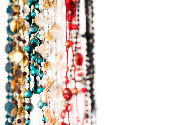 An abstract closeup of colourful beaded necklaces hanging in a row against a white background, with negative white space to the right of the necklaces	