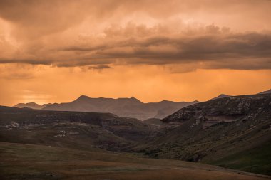 Güney Afrika, KwaZulu Natal 'daki Golden Gate Highlands Ulusal Parkı' ndan görülen Amphitiyatronun etrafındaki Drakensberg dağları üzerinde gün batımında dramatik fırtına altın parlıyor.