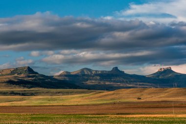 Amfitiyatro ve etrafındaki dağlar mavi ve bulutlu bir gökyüzünün altında akşam güneşinin aydınlattığı renkli ovalarla dolu bir vadi. Drakensberg, Güney Afrika