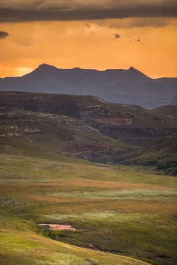Drakensberg, Güney Afrika 'daki Drakensberg' deki Golden Gate Highlands Ulusal Parkı 'ndan görülen Amfitiyatronun etrafındaki Drakensberg dağları üzerinde dramatik fırtına bulutları gün batımında altın parlıyor.