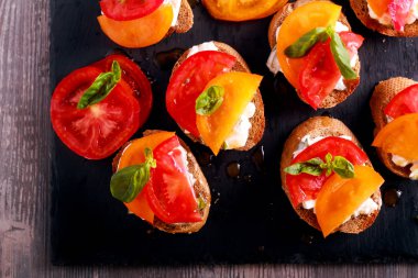 Kara tahta üzerinde peynir ve fesleğen tepesinde domates bruschetta