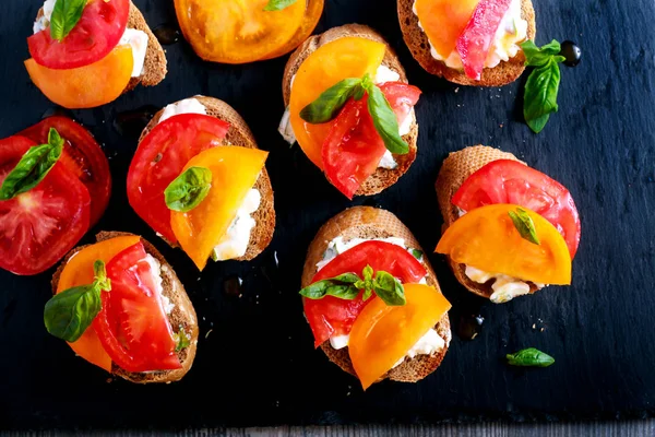 Cheese and basil tomato topped bruschetta on black board — Stock Photo, Image
