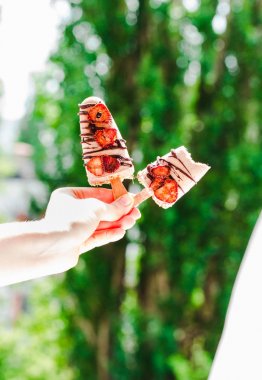 Çikolata ve strawberri ile bir dondurma çubuklu dondurmayı tutan el