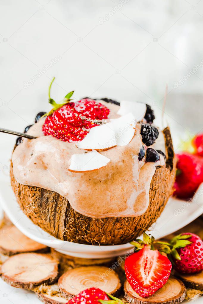 Melting chocolate ice cream with berries on coconut cup.