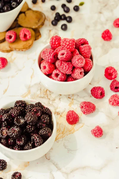 Raw raspberries and wild black, blackberries in white cups. Ligh — Stock Photo, Image