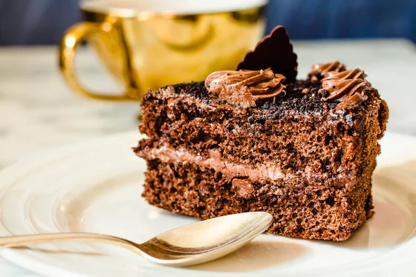 Un pedazo de pastel de chocolate en un plato blanco y una taza de café de oro , — Foto de Stock