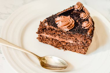 Beyaz tabakta bir parça çikolatalı kek ve bir fincan altın kahve.,