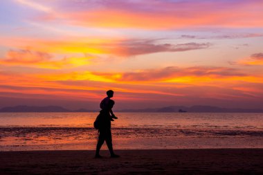Babası oğlunun boynunda taşıyan deniz arka plan üzerinde batımında sahilde yürüyor. siluet stil