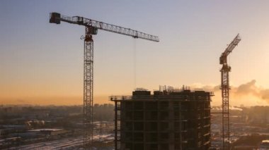 Yüksek katlı apartmanın 4 k batan güneşin - İnşaat vinçleri ve işçi etkin çalışma arka plan üzerinde kış inşaatı