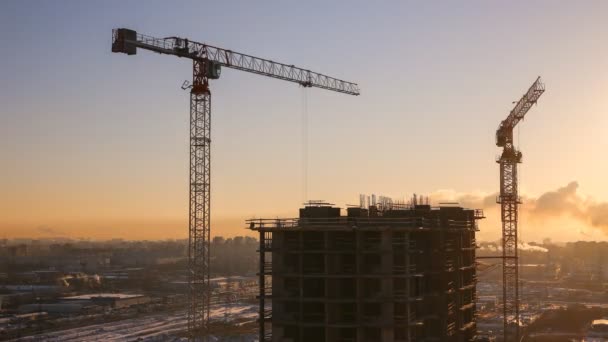 Zimní výstavba výškové činžovního domu v rozlišení 4k na pozadí zapadajícího slunce - aktivní práce stavební jeřáby a pracovníků