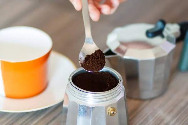 Hand holds a spoon with ground coffee before pouring it into the coffee maker