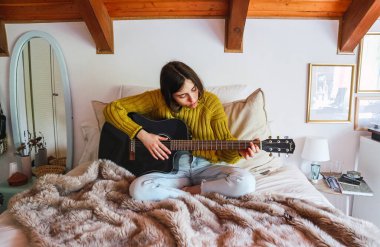 Yatakta siyah gitar çalan genç bir kadın.