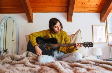 Yatakta siyah gitar çalan genç bir kadın.